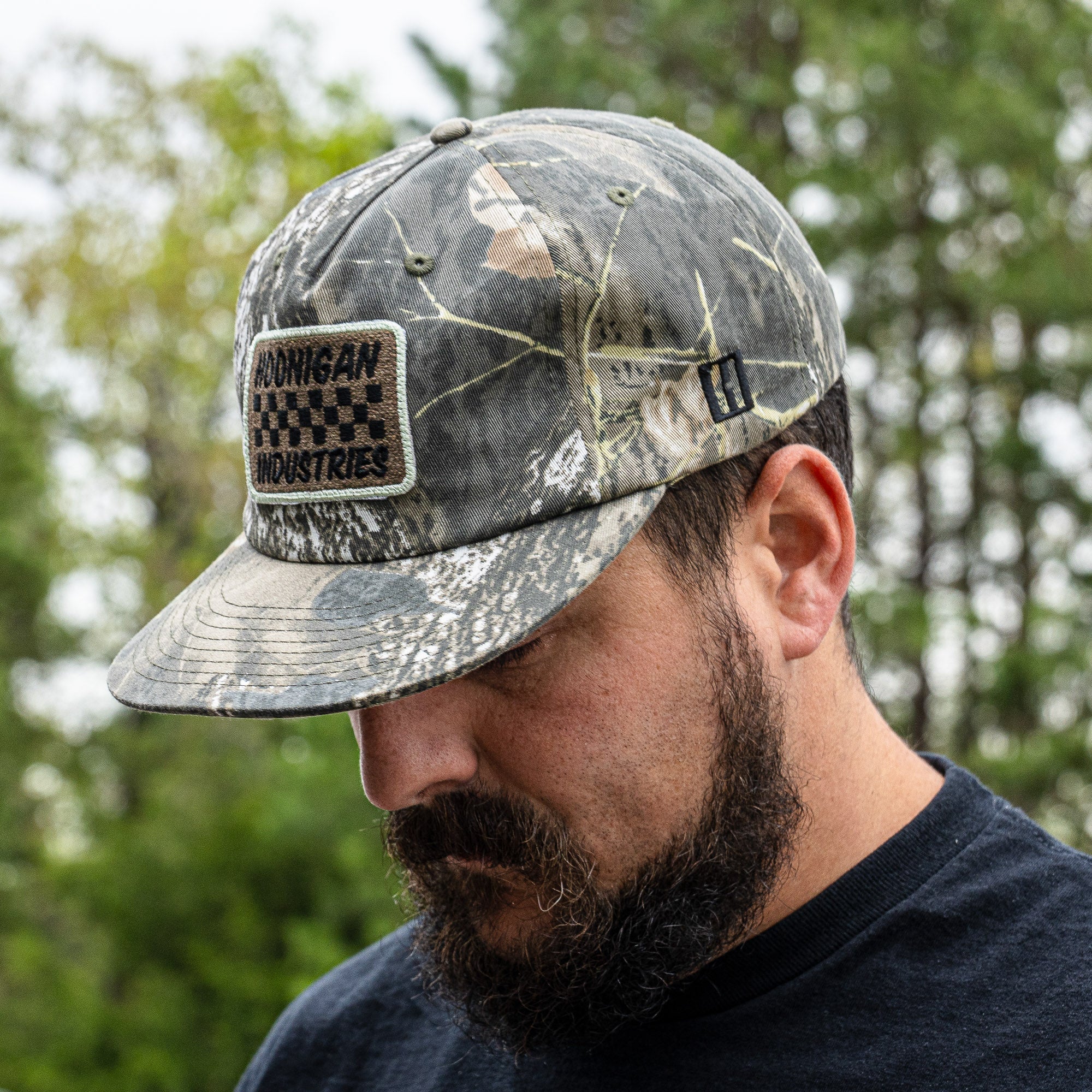 Hoonigan SPRINT unstructured snapback hat in camo design worn by a man outdoors, showcasing its stylish and rugged appeal.