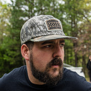 Hoonigan SPRINT unstructured snapback hat worn by a man with a beard, featuring a camouflage design and logo patch.