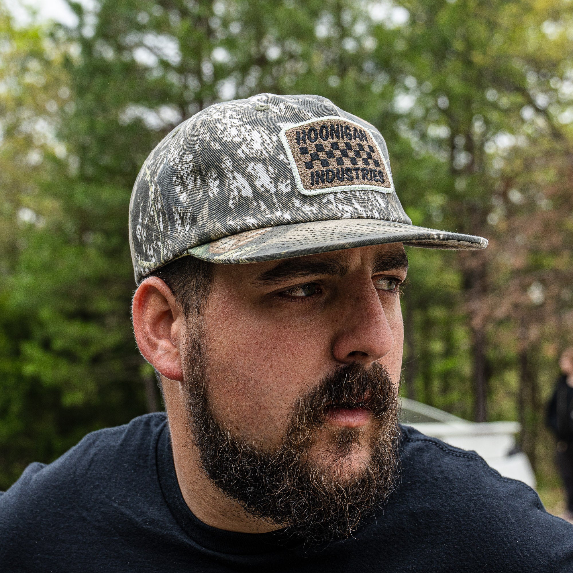 Hoonigan SPRINT unstructured snapback hat worn by a man with a beard, featuring a camouflage design and logo patch.