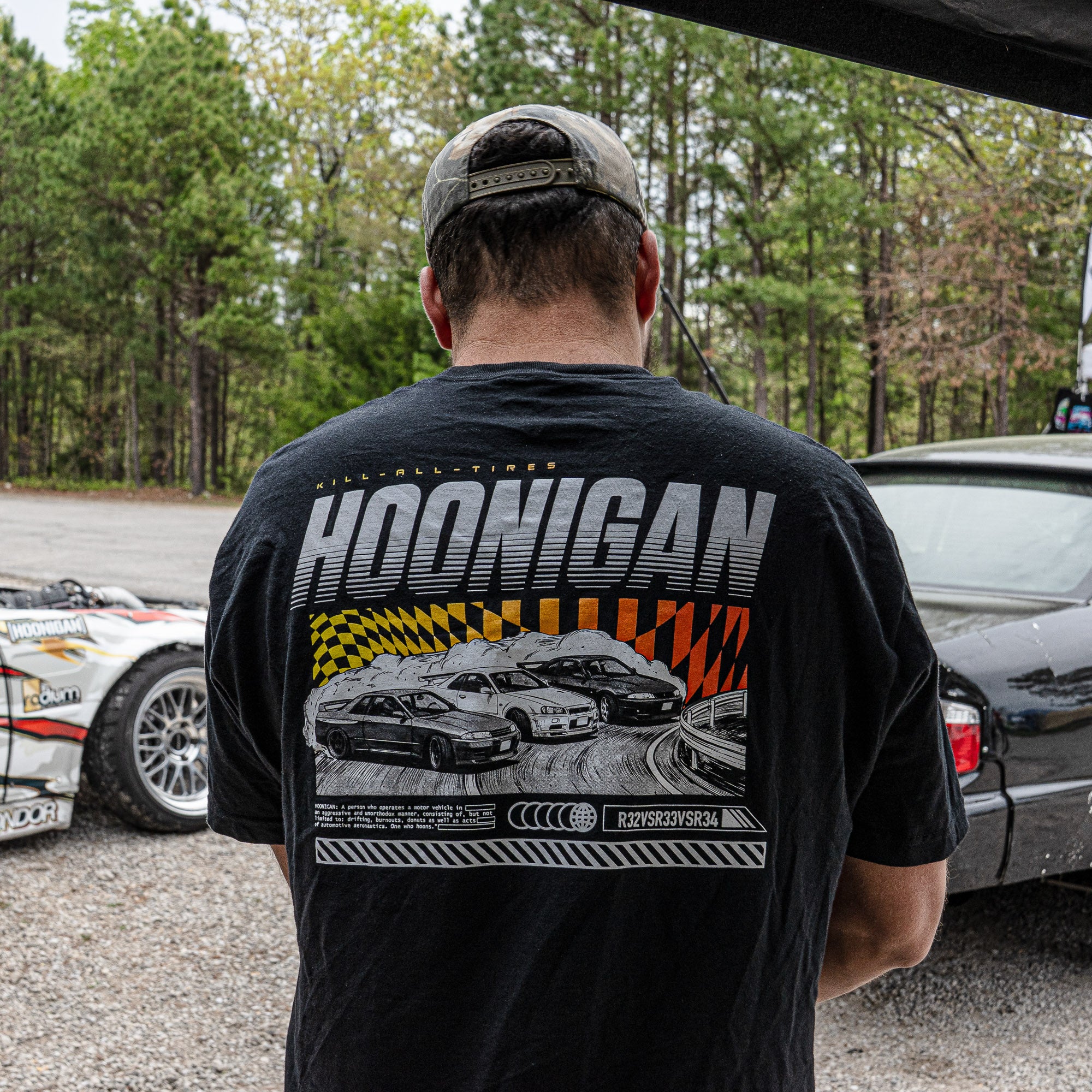 Man wearing a black Hoonigan SLIDEWAYS short sleeve T-shirt featuring a graphic of racing cars on the back.