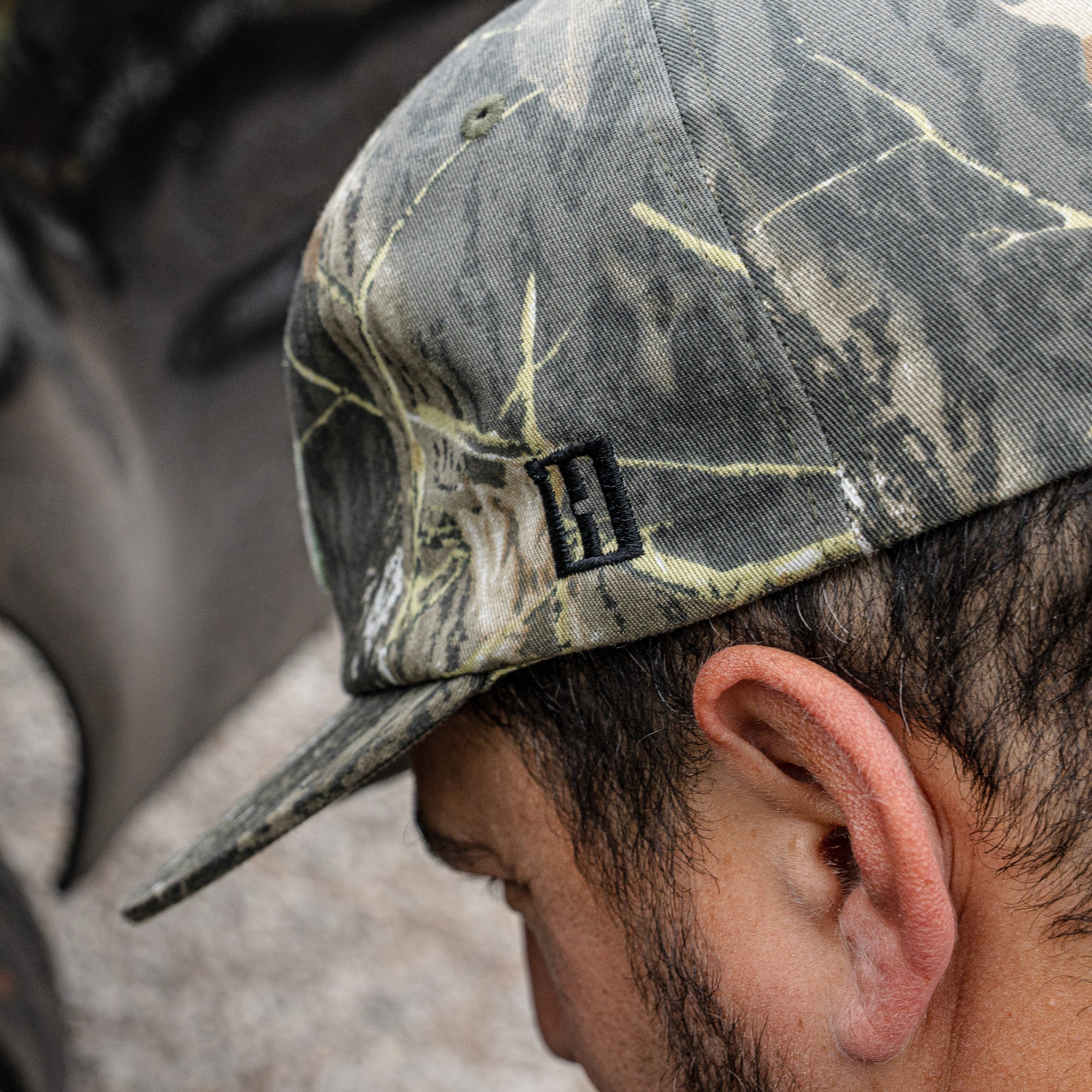Hoonigan SPRINT unstructured snapback hat in camouflage pattern, worn by a person with short hair outdoors.