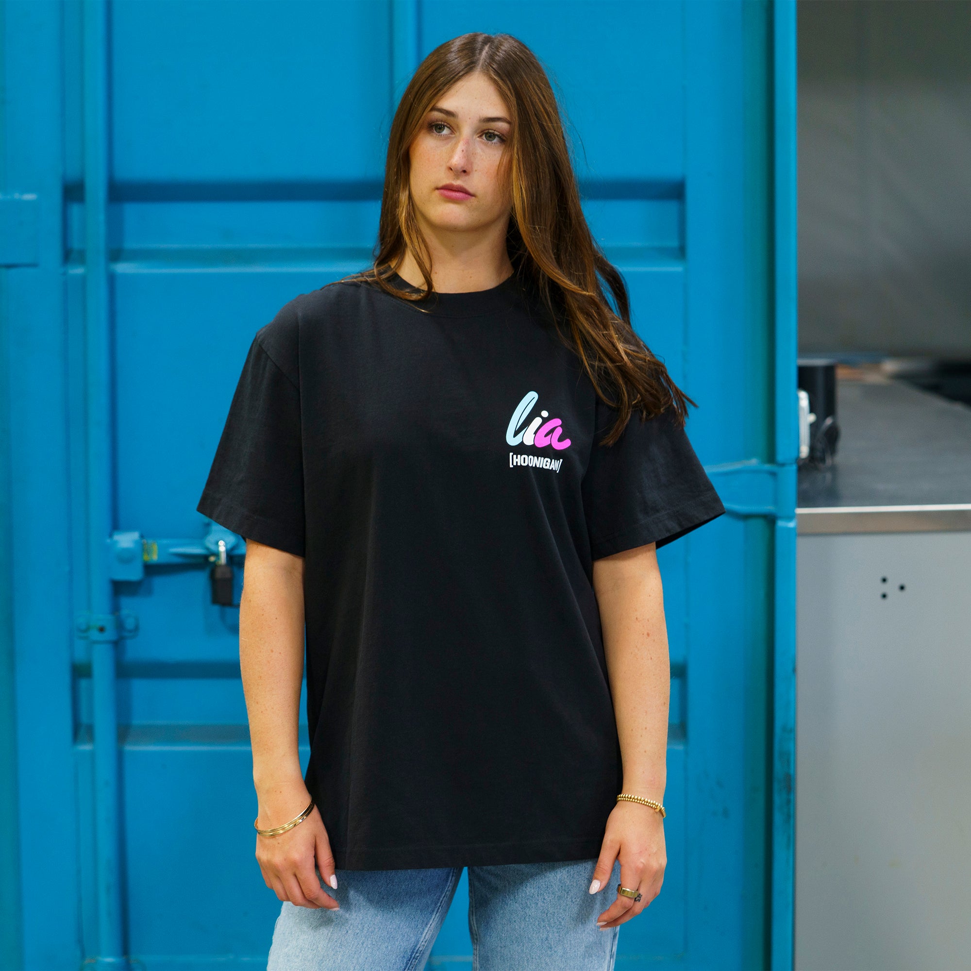 Model wearing a black Hoonigan x Lia Block DSC short sleeve premium tee, showcasing a stylish and casual automotive lifestyle look.