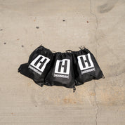 Black drawstring bags with Hoonigan logo, showcasing the $55 Grab Bag containing three shirts for automotive enthusiasts.