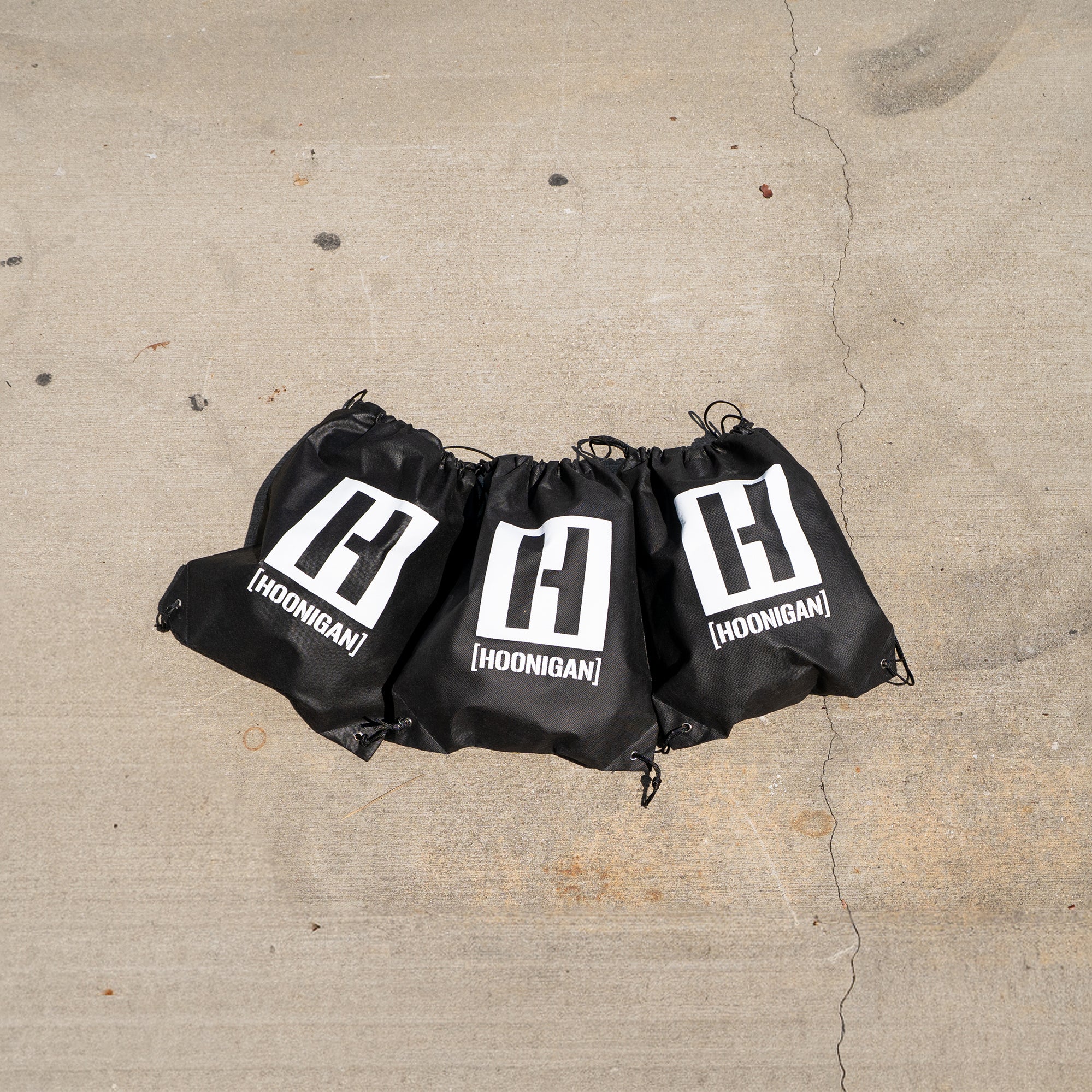 Hoonigan grab bags featuring shirts, hoodies, hats, and bags, designed for motorsport enthusiasts and car culture fans.