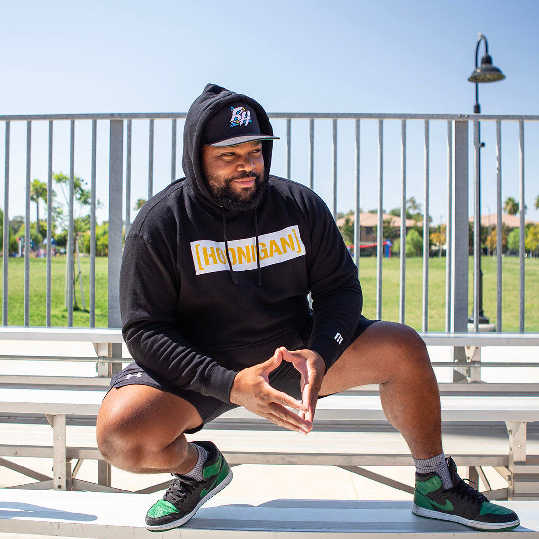 Hoonigan GAME DAY hoodie in black and yellow, featuring a front pouch pocket and bold graphics, modeled in a casual outdoor setting.