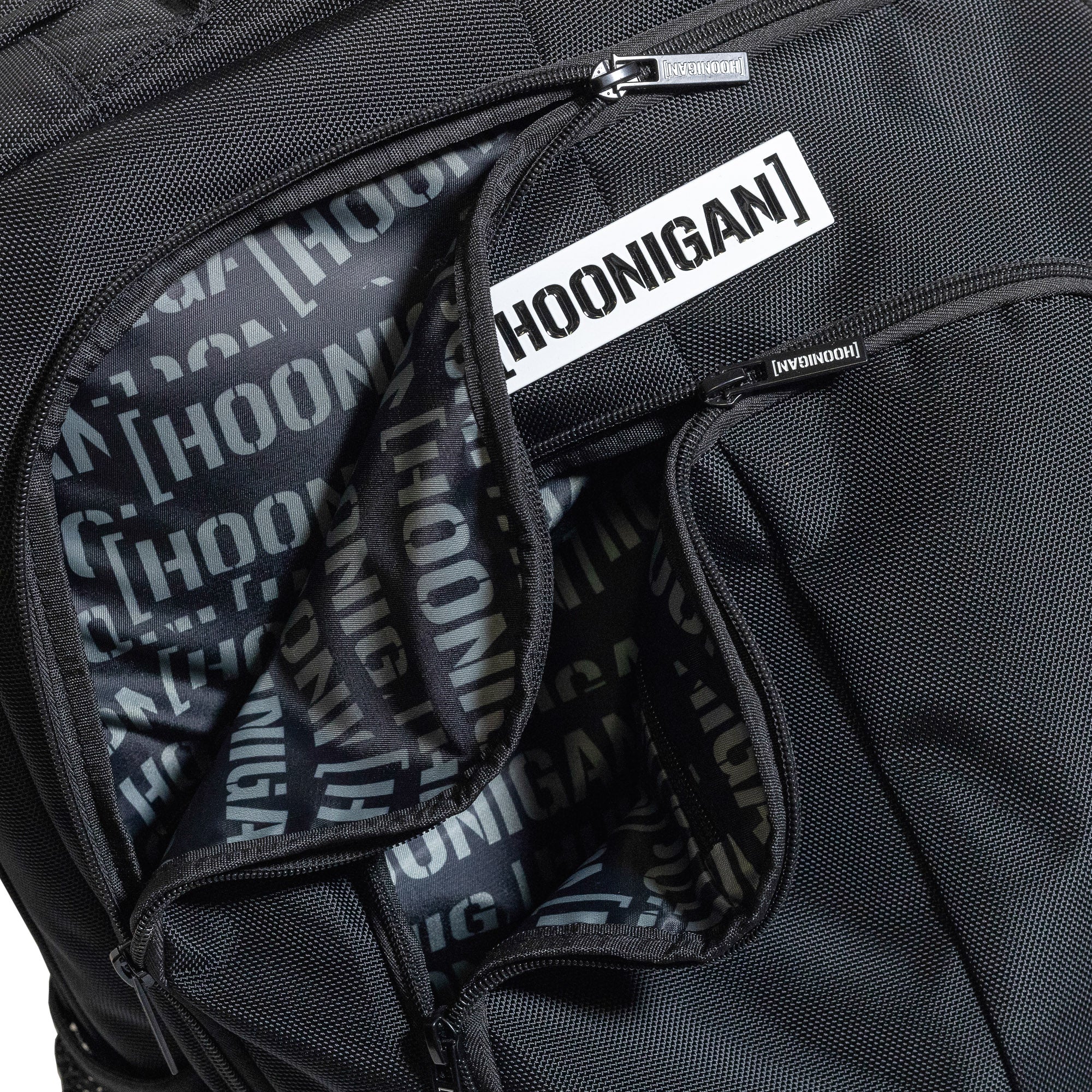 Hoonigan METAL BAR Backpack featuring a sleek black design with a prominent logo and multiple compartments.