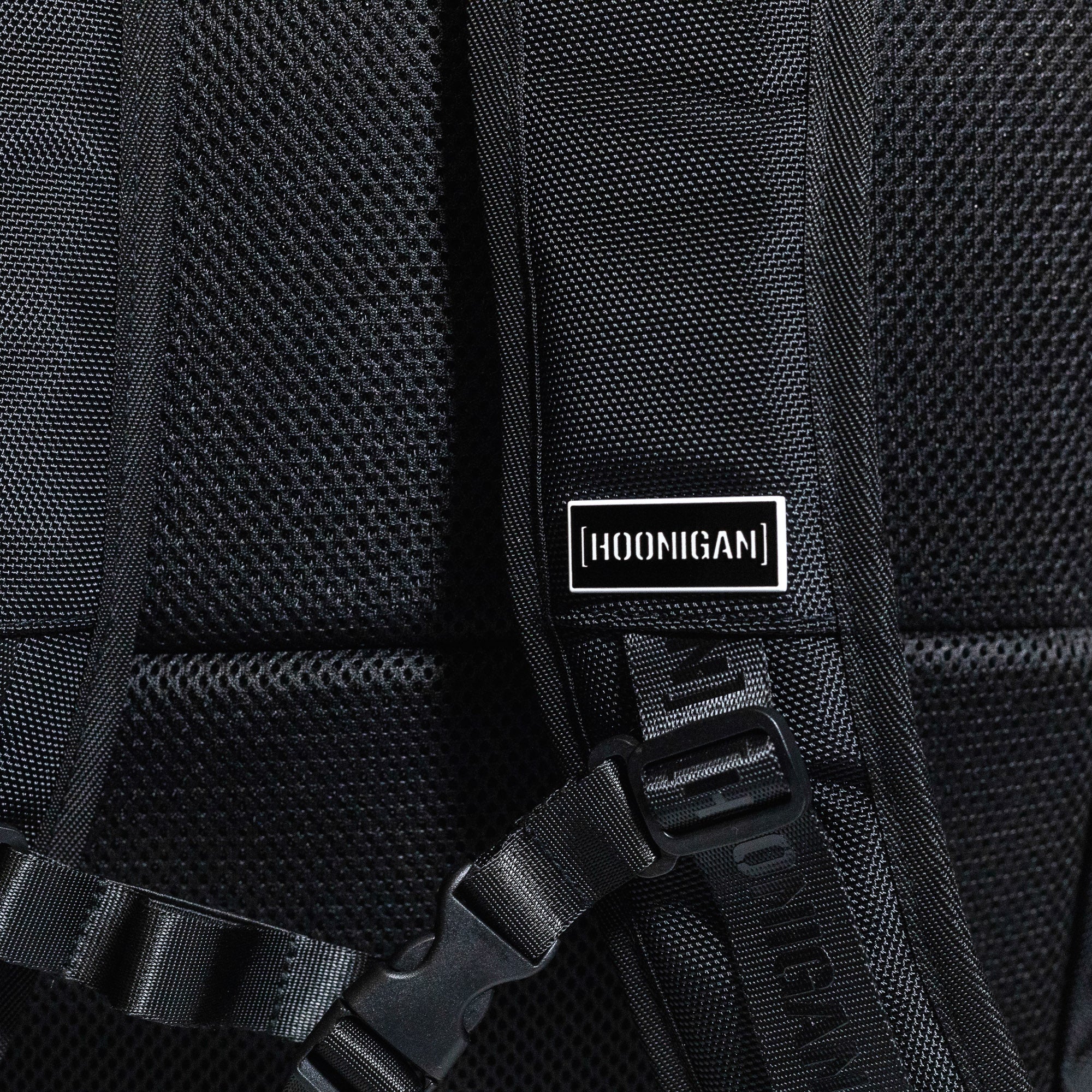 Hoonigan METAL BAR Backpack featuring a sleek black design with a front mesh pocket and adjustable straps.