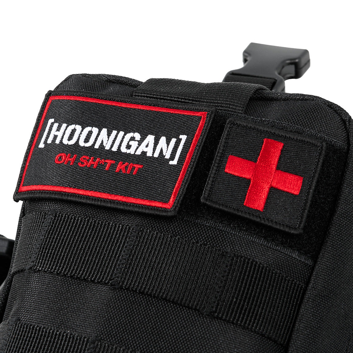 Close-up of the Hoonigan OH SH*T Safety Kit with black fabric, red cross patch, and embroidered label on a vehicle safety bag.