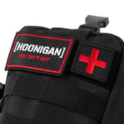 Close-up of the Hoonigan OH SH*T Safety Kit with black fabric, red cross patch, and embroidered label on a vehicle safety bag.