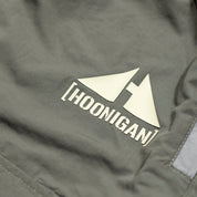 Close-up of gray cargo shorts with a rain-activated Hoonigan logo featuring two stylized triangles and bold text.