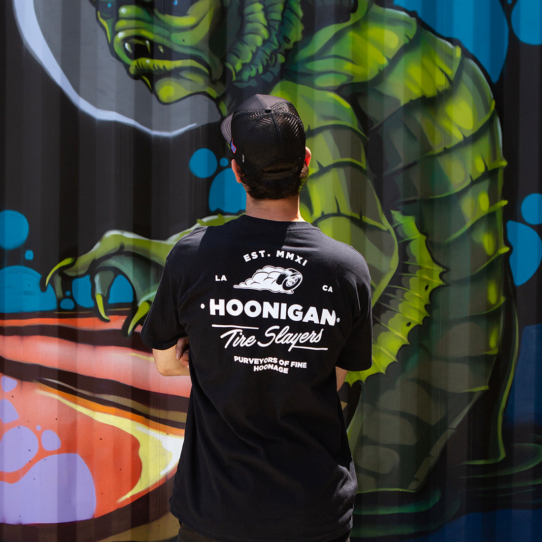 Hoonigan CHEATER SLICKS Short Sleeve Tee, black, featuring a logo graphic on the back, styled in a lifestyle setting.