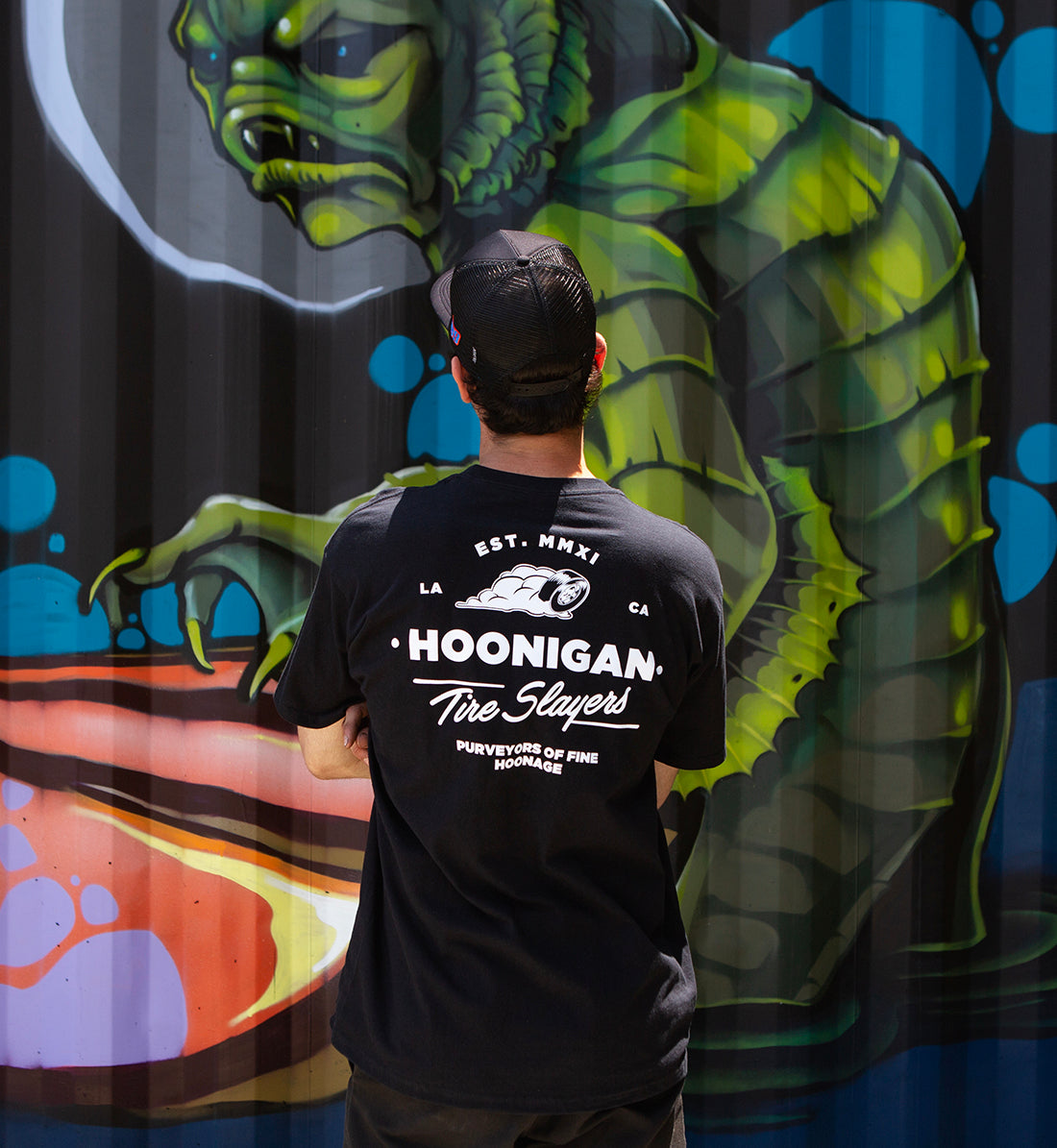 Hoonigan CHEATER SLICKS Short Sleeve Tee, black, featuring a logo graphic on the back, styled in a lifestyle setting.