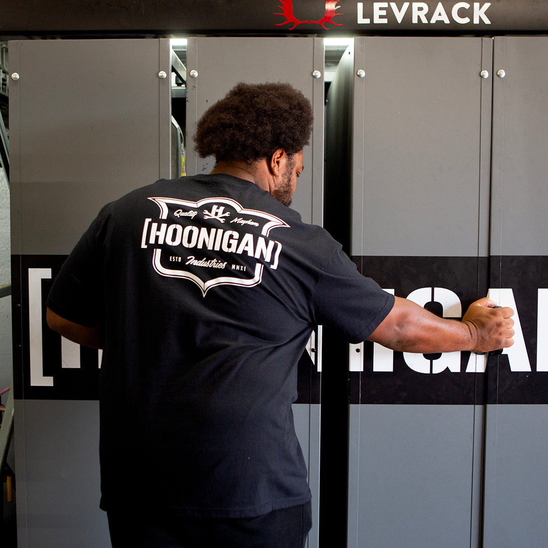 Hoonigan EMBLEM Short Sleeve Tee in black featuring a bold logo on the back, styled on a model outdoors.