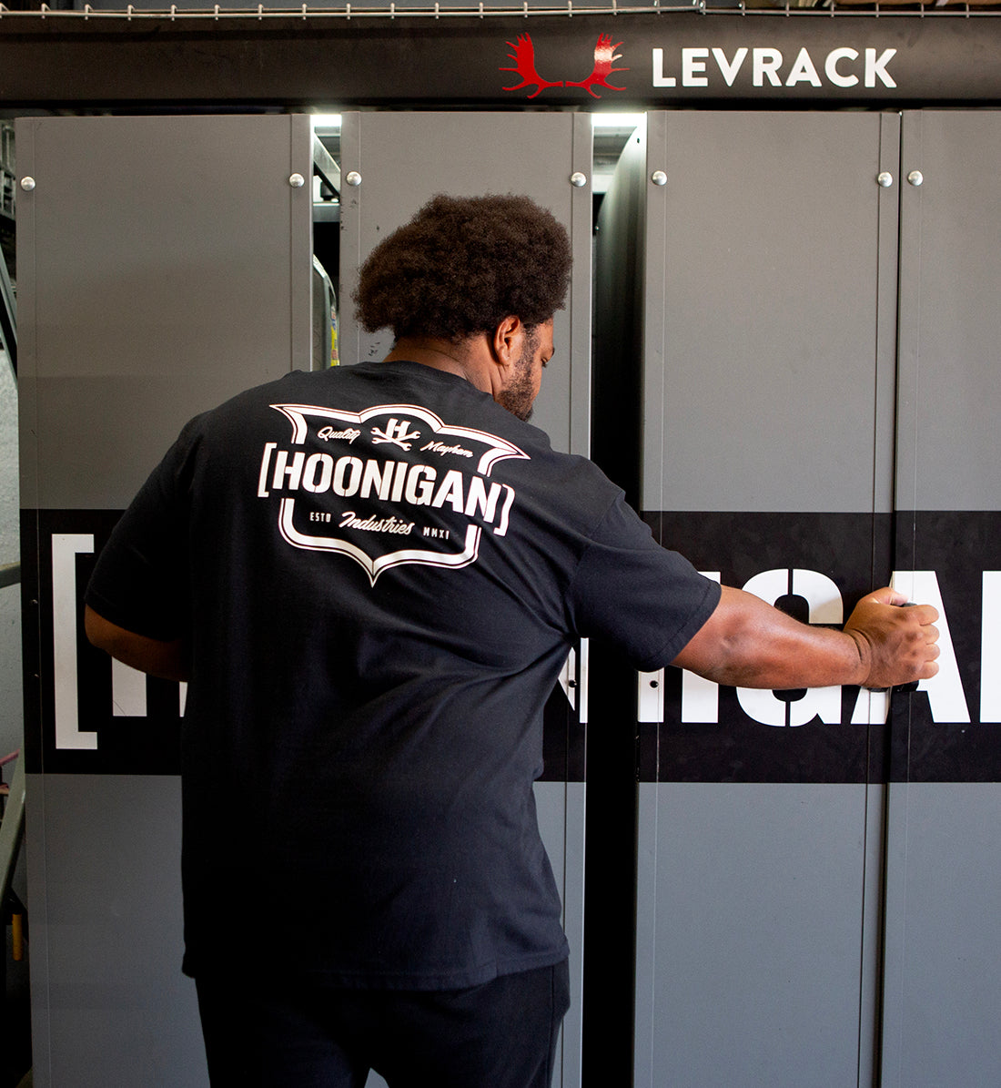 Hoonigan EMBLEM Short Sleeve Tee in black featuring a bold logo on the back, styled on a model outdoors.