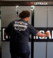 Hoonigan EMBLEM Short Sleeve Tee in black featuring a bold logo on the back, styled on a model outdoors.