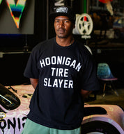 Black Hoonigan TIRE SLAYER short sleeve t-shirt displayed in a lifestyle setting, featuring a large front graphic of the "TIRE SLAYER" logo.