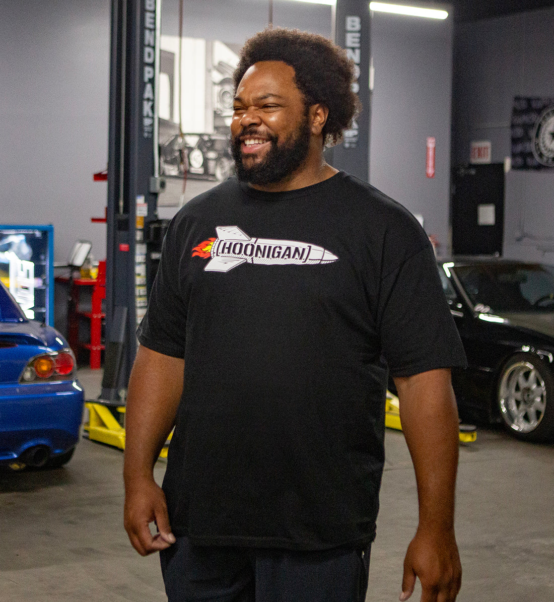 Hoonigan ROCKET Short Sleeve Tee featuring a vibrant graphic design on a black background, model wearing the shirt outdoors.