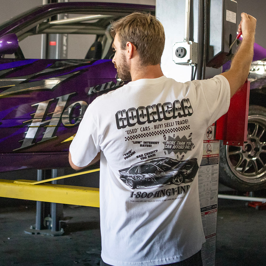 Hoonigan USED CARS Short Sleeve Tee in white, featuring a lifestyle image showing the back design.