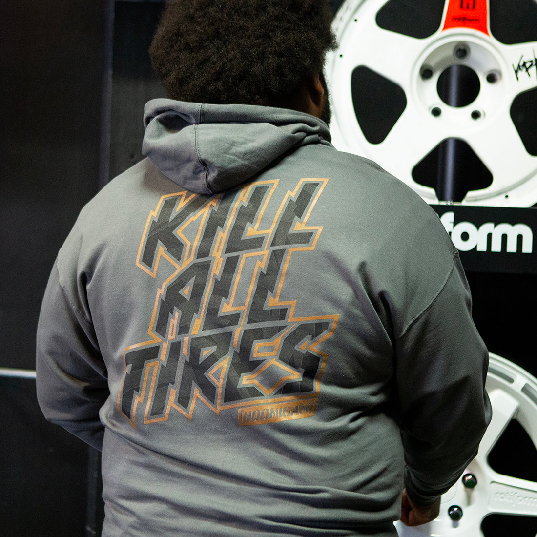 Hoonigan GYMKHANA7 KILL ALL TIRES pullover hoodie in black, featuring a graphic print on the back, being worn outdoors.