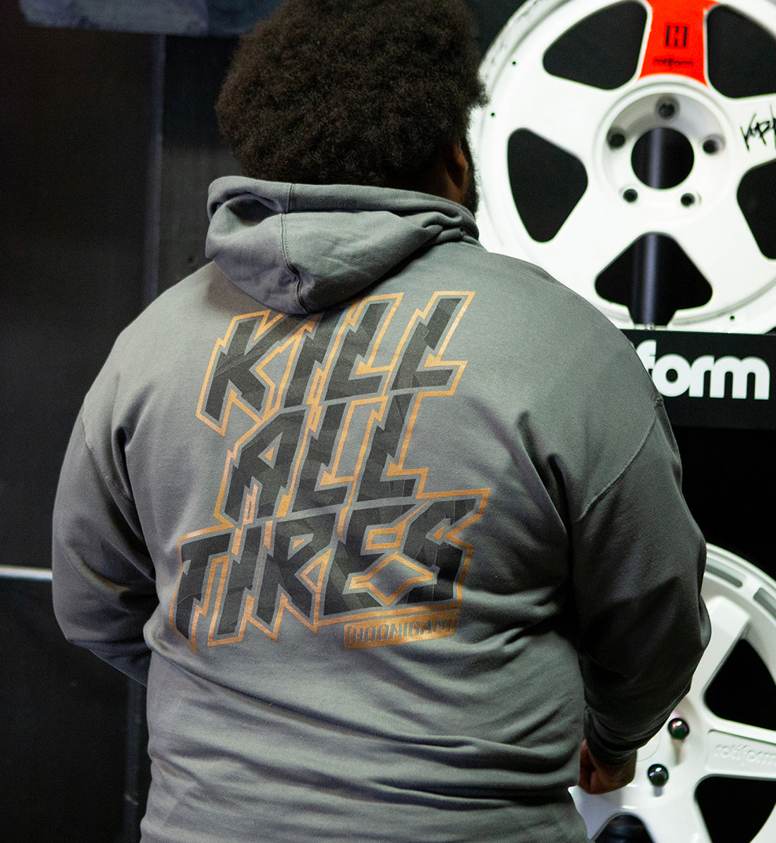 Hoonigan GYMKHANA7 KILL ALL TIRES pullover hoodie in black, featuring a graphic print on the back, being worn outdoors.