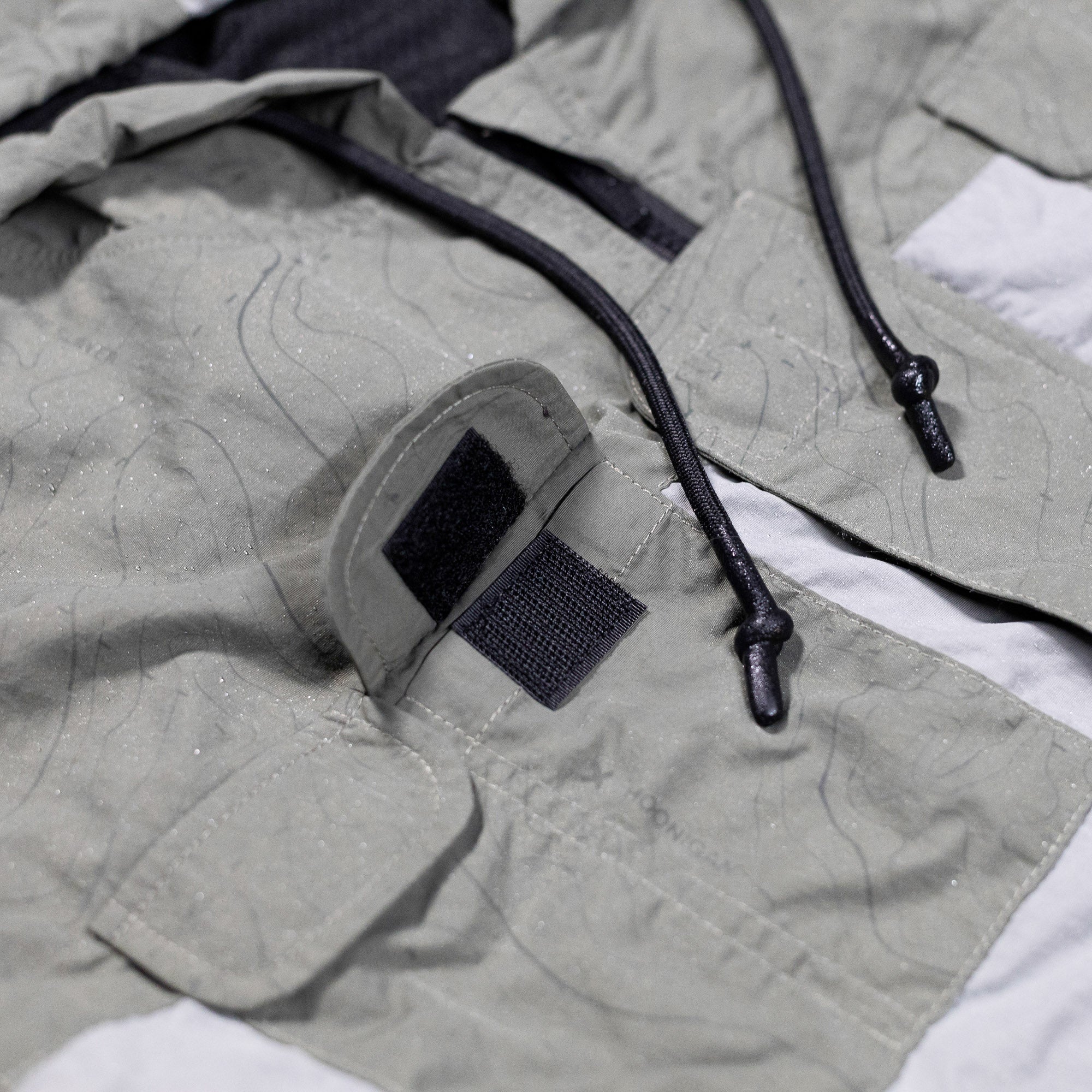 Close-up of the Hoonigan H.A.V.O.C. rain-activated windbreaker jacket showing adjustable velcro strap, drawstrings, and water-resistant fabric.