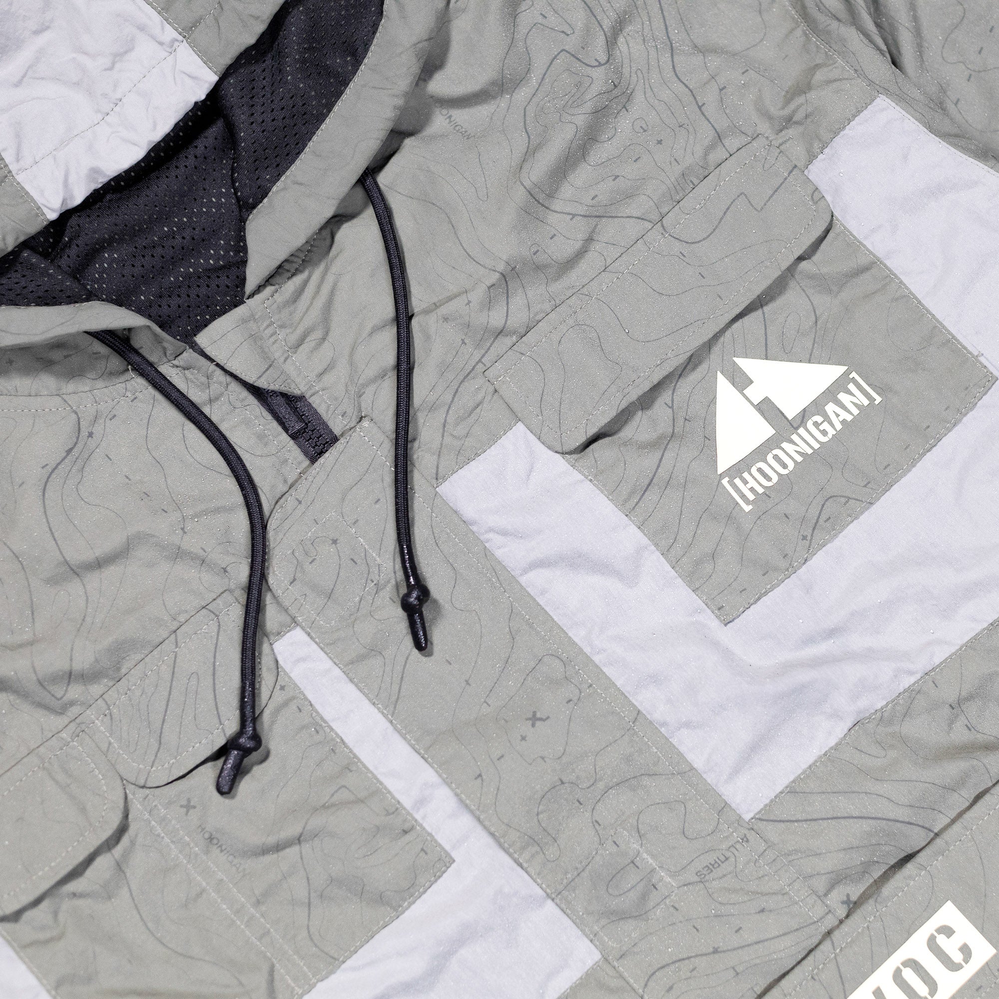 Hoonigan H.A.V.O.C. rain-activated windbreaker jacket with a gray color, black drawstrings, and a white logo patch on the front.