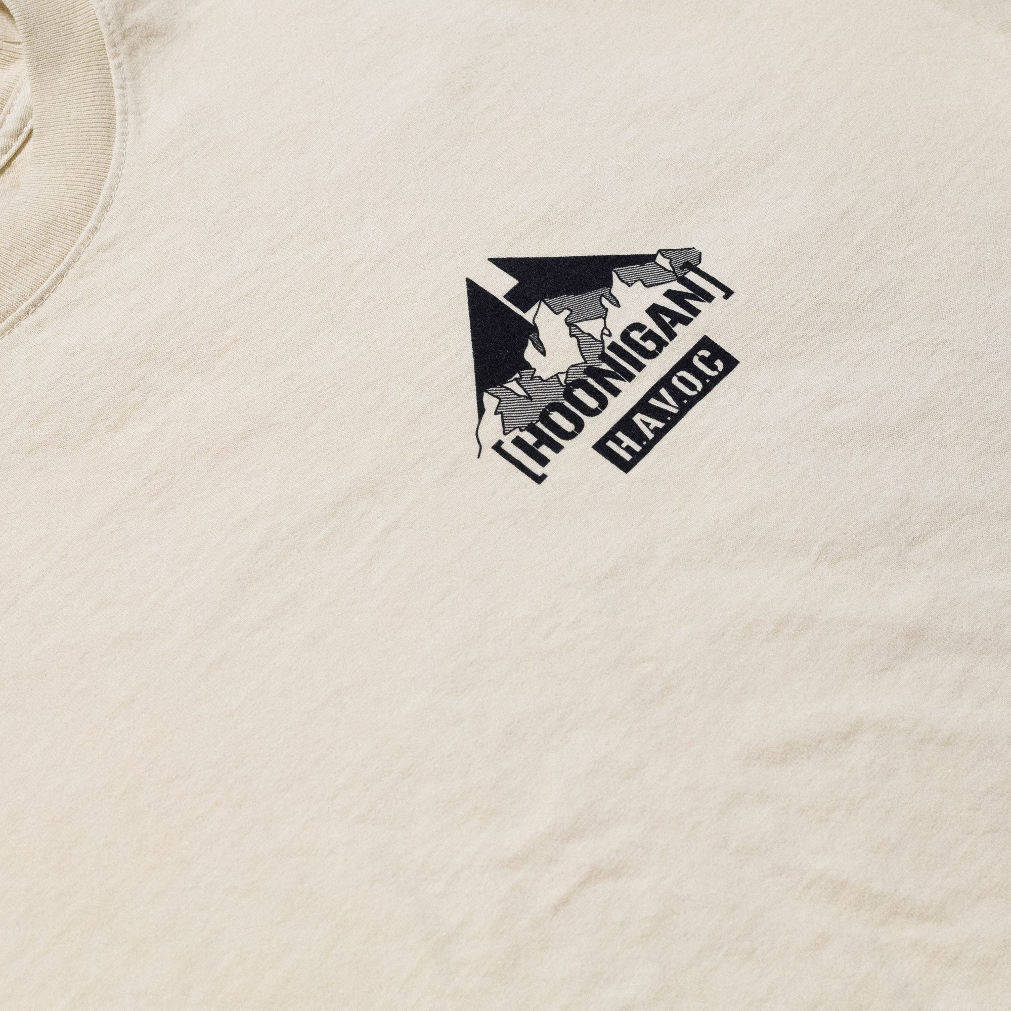 Close-up of a beige Hoonigan SAFARI short sleeve tee featuring a black and white graphic logo on the chest.