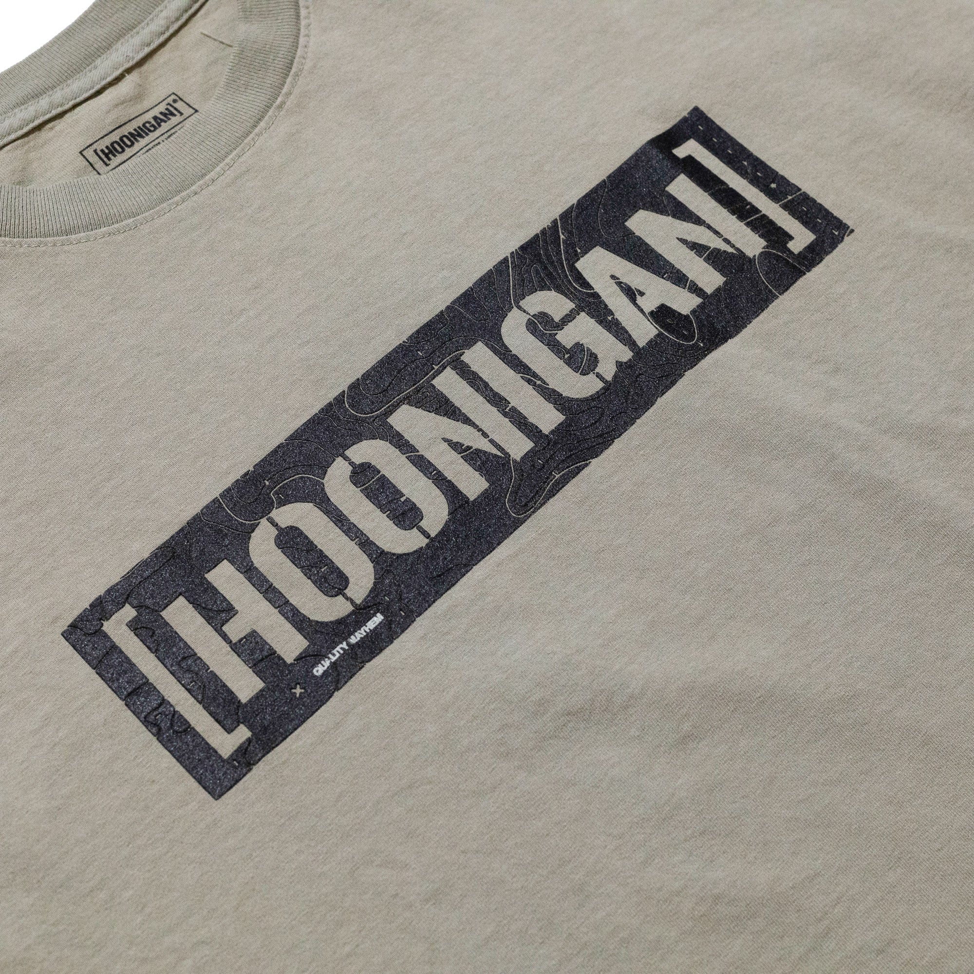 Beige T-shirt with a black rectangular graphic reading "HOONIGAN" in bold, distressed font across the chest.