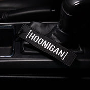Hoonigan CENSOR BAR Jet Tag Keychain resting on a car console, showcasing its bold embroidered logo.