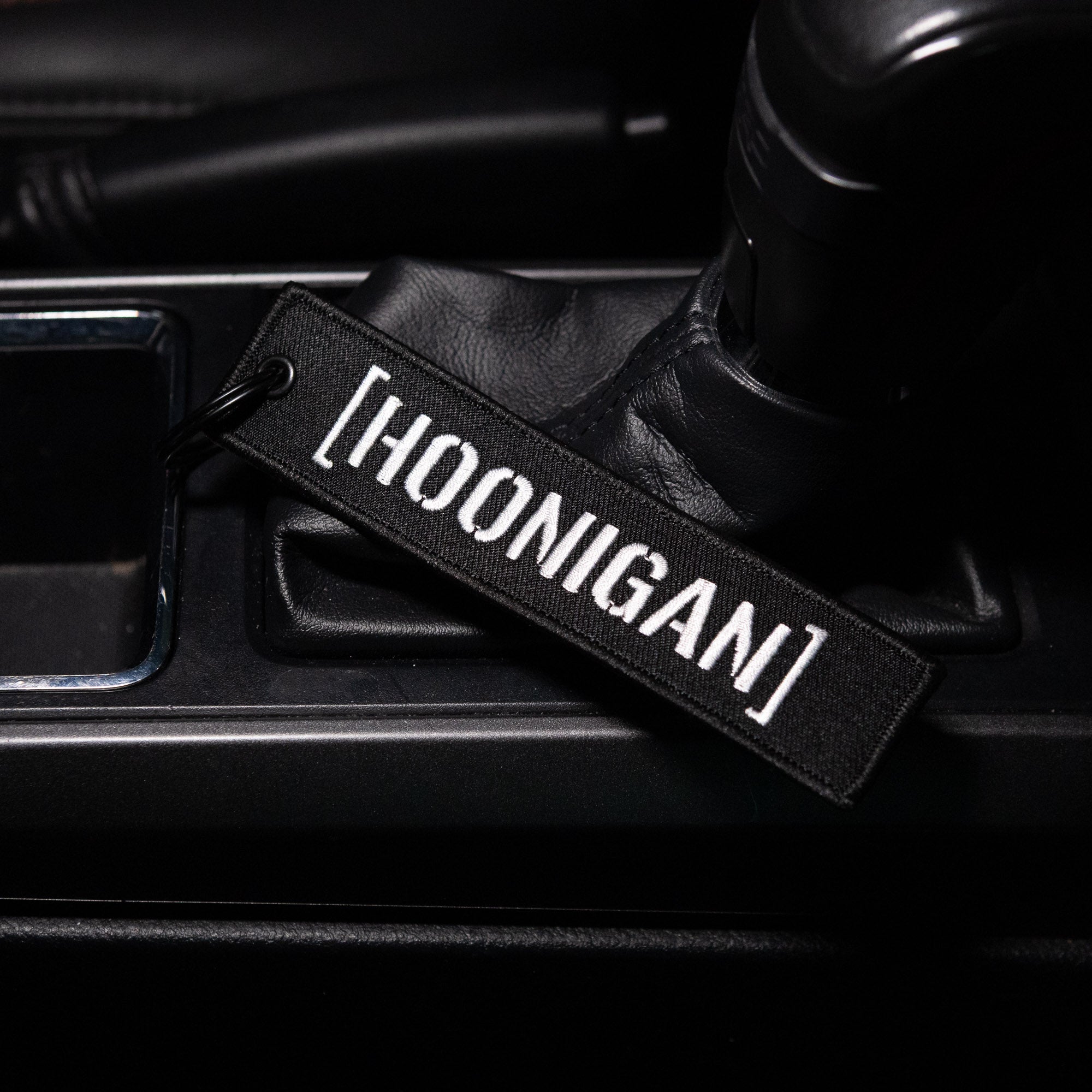 Hoonigan CENSOR BAR Jet Tag Keychain resting on a car console, showcasing its bold embroidered logo.