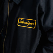 Hoonigan KNUCKLEBUSTERS black jacket featuring a bold logo on the back and front, designed for motorsport enthusiasts.