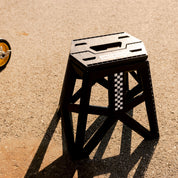 Hoonigan TRACK DAY collapsible stool with a logo, black fabric seat, and sturdy metal frame, designed for outdoor use.