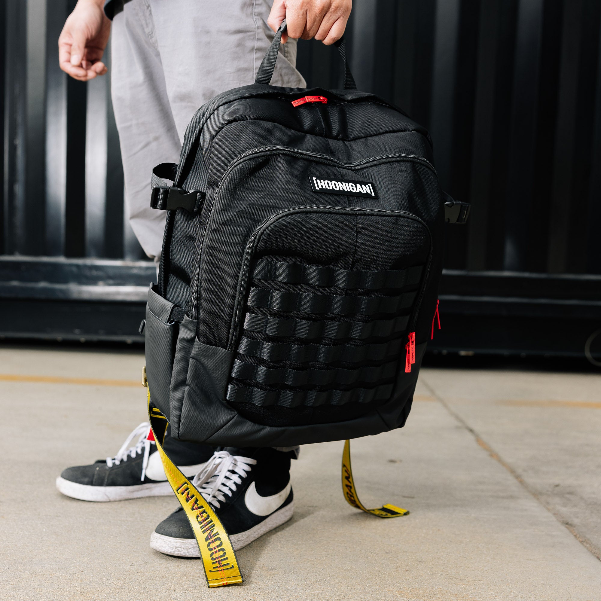 Hoonigan Ratchet Strap Backpack in black with a bold logo and durable straps, featuring multiple compartments and a stylish design.