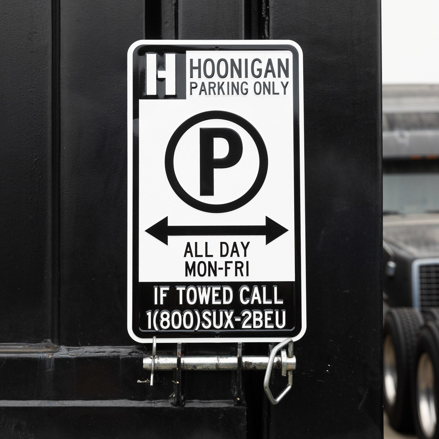 Hoonigan PARKING ONLY sign with bold black and white lettering on a weathered background.