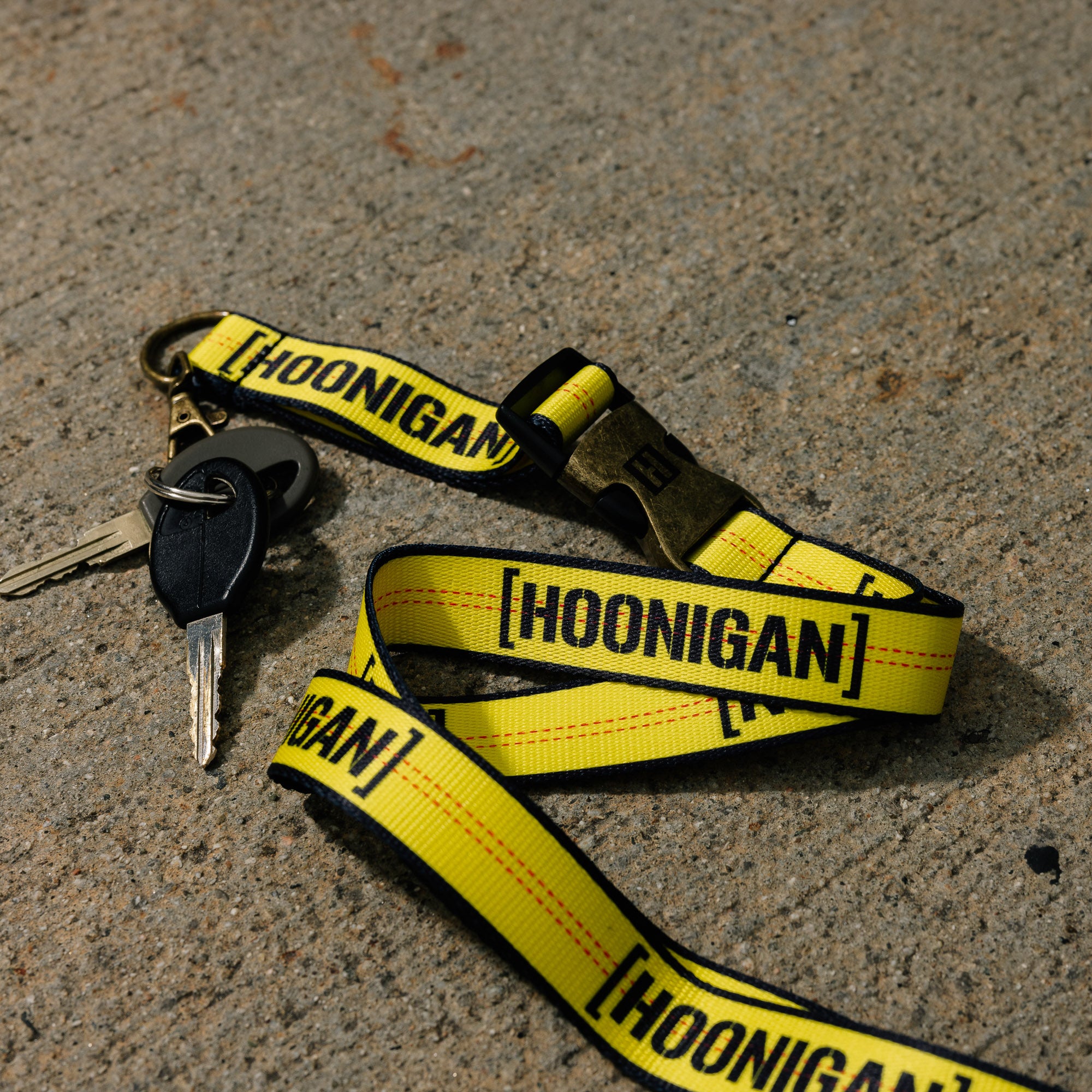 Hoonigan Ratchet Strap Lanyard featuring bold black and white branding, durable material, and metal clasp.