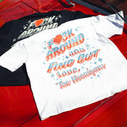 White and black Hoonigan FIND OUT V2 short sleeve tees with colorful, retro-style text and star graphics, laid on a red surface.