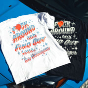 Two Hoonigan FIND OUT V2 short sleeve T-shirts, one white and one black, with bold graphic text and star designs, laid on a blue car.