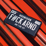 Black license plate with white text reading "FCK ARND" and "and find out," featuring a "Hoonigan" logo and a small sticker in the corner.