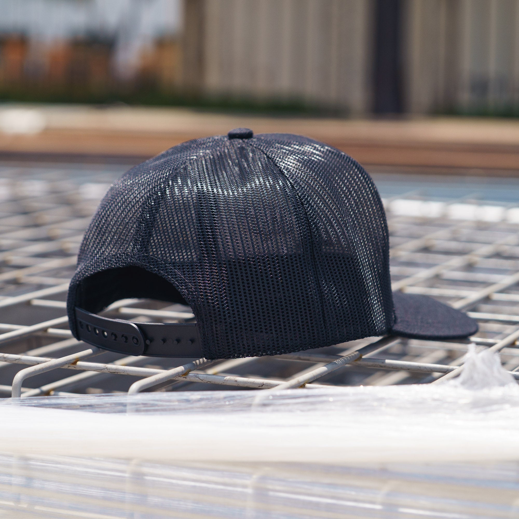 Back of black mesh snapback trucker hat with adjustable snap closure, and curved brim.