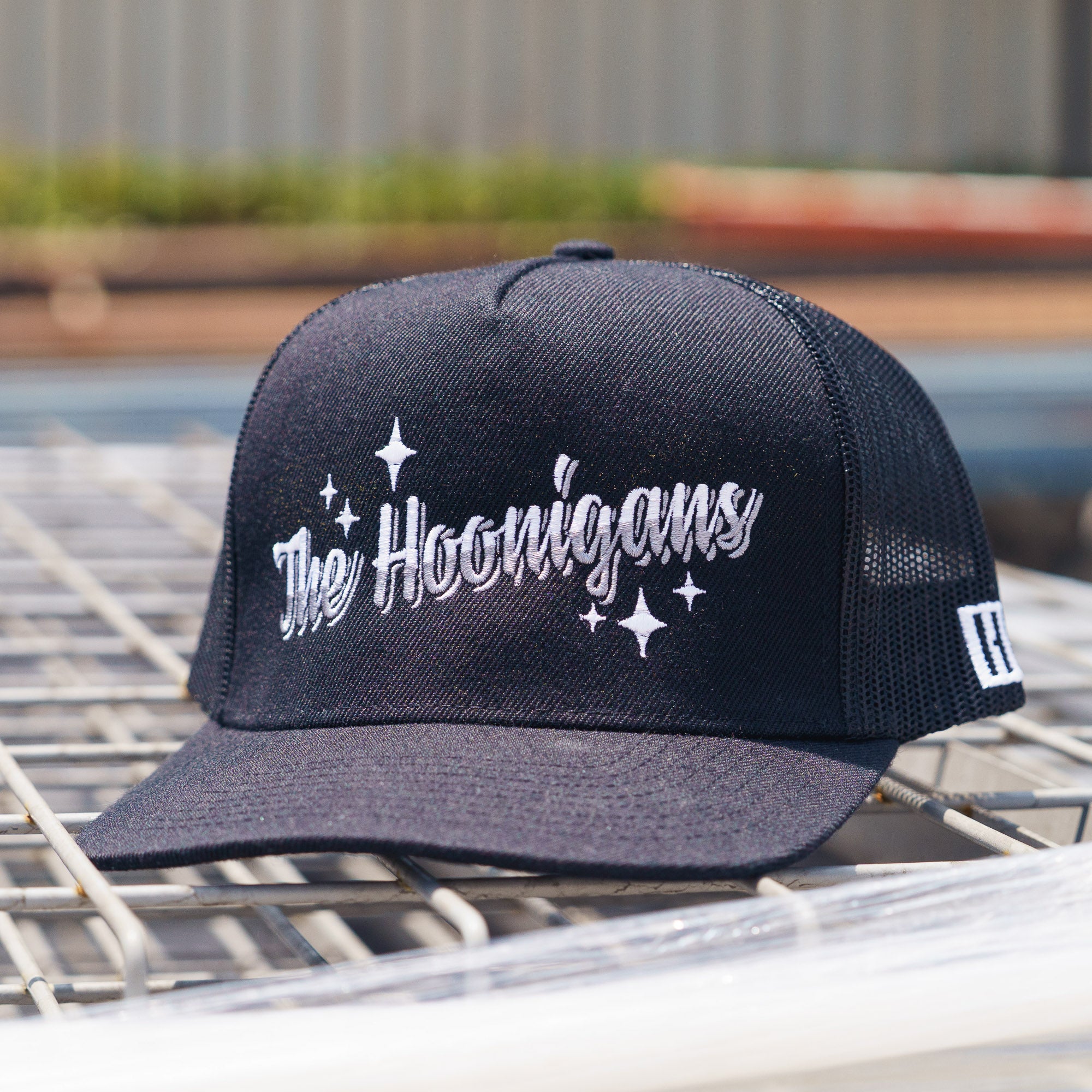 Black snapback trucker hat with "The Hoonigans" embroidered in white, featuring star accents and mesh back panels.
