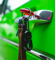 Hoonigan FOUND IT Keychain attached to a leather strap, hanging from a chrome car door handle on a vibrant green vehicle.