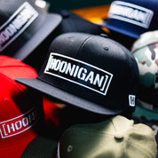 Hoonigan CENSOR BAR Snapback Hat in black surrounded by various colors and styles, showcasing automotive lifestyle apparel.