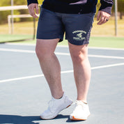 Black Hoonigan TRACK TEAM athletic shorts with a white logo, featuring an elastic waistband and side pockets, displayed on a wooden surface.