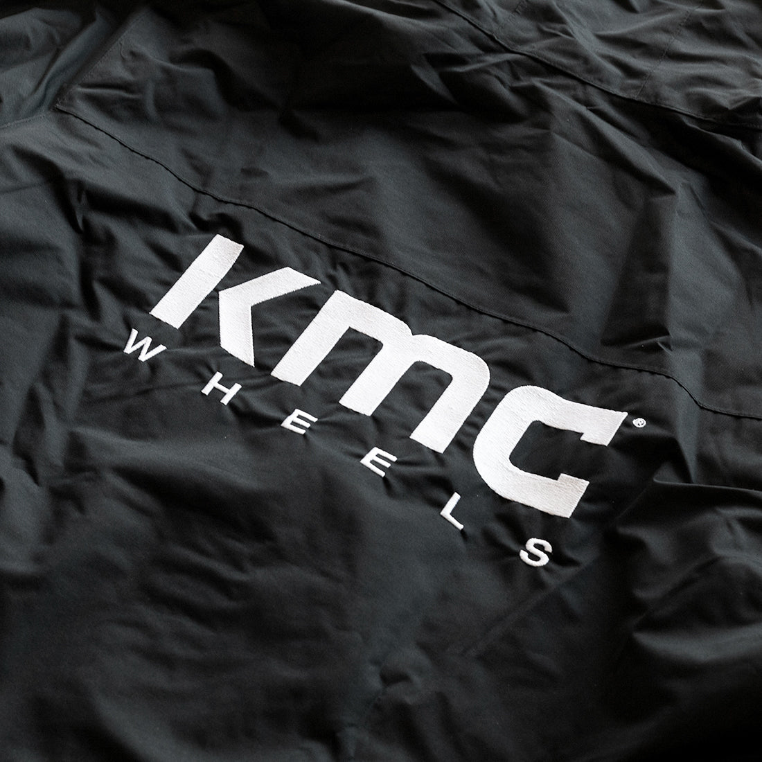 Alt text: KMC jacket featuring a sleek black design, zippered front, and stylish hood with drawstrings, displayed on a neutral background.