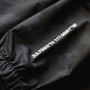 Close-up of a black Rotiform GLOBAL IMPACT half zip anorak jacket with white printed coordinates and text on the fabric.