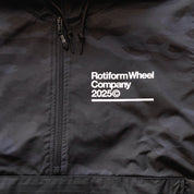 Close-up of a black Rotiform GLOBAL IMPACT Half Zip Anorak Jacket with white text, zipper, and drawstrings on the collar.
