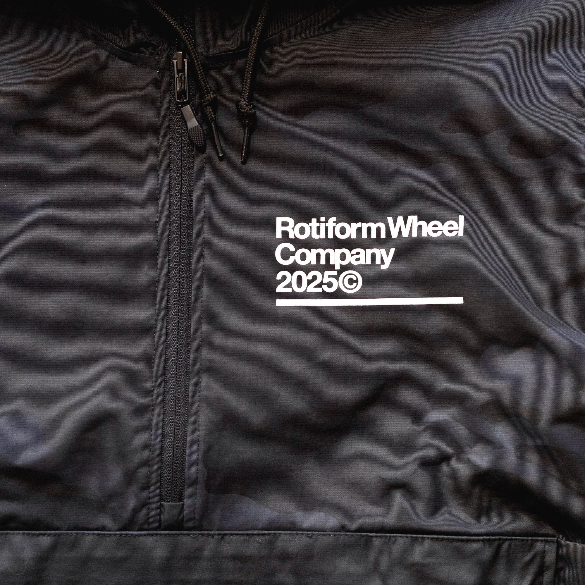 Close-up of a black Rotiform GLOBAL IMPACT Half Zip Anorak Jacket with white text, zipper, and drawstrings on the collar.