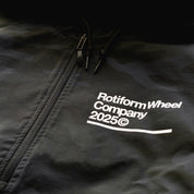 Close-up of a black Rotiform GLOBAL IMPACT half zip anorak jacket with a front zipper, drawstrings, and white printed branding.