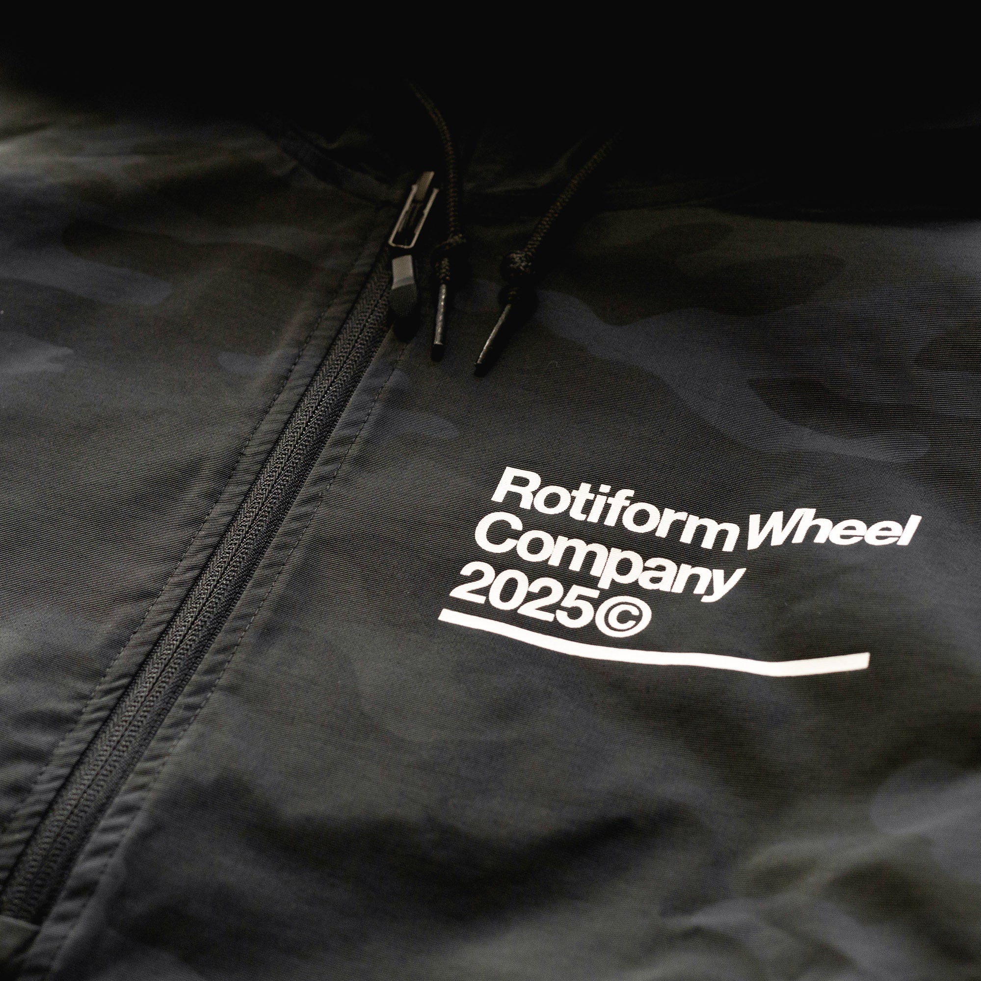 Close-up of a black Rotiform GLOBAL IMPACT half zip anorak jacket with a front zipper, drawstrings, and white printed branding.