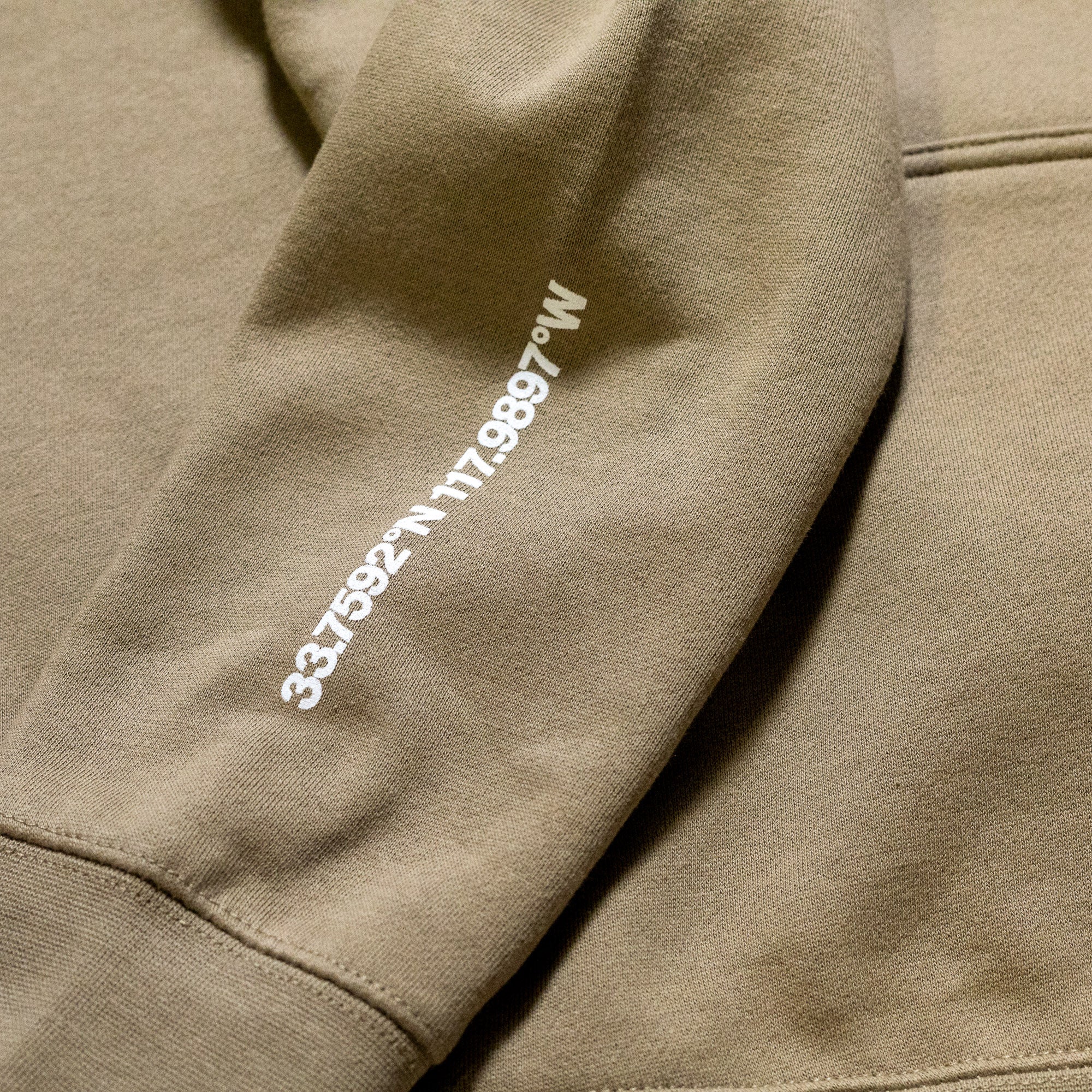 Beige hoodie featuring white printed text with a product code and brand name on the sleeve.